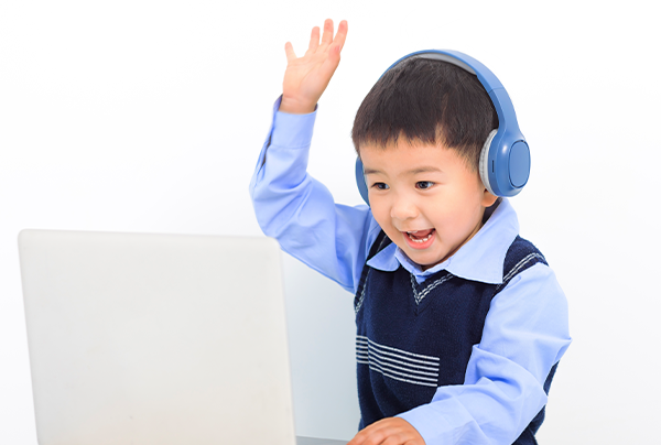 戴著耳機面向電腦，開心地舉起手說話的男孩