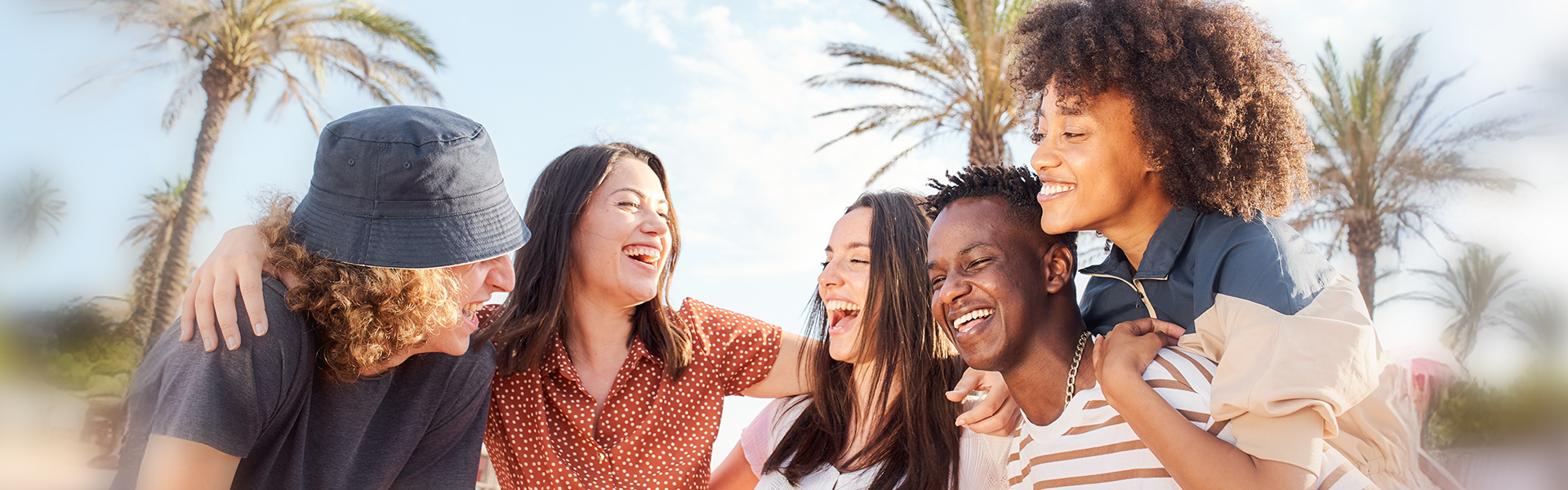 海外留学中に友情を深める多国籍の学生たち|青空とヤシの木に囲まれた笑顔のグループショット