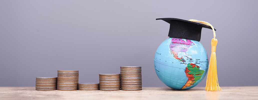 最低価格で留学を実現|学帽をかぶった地球儀と積み重なるコインで費用の安さを表現