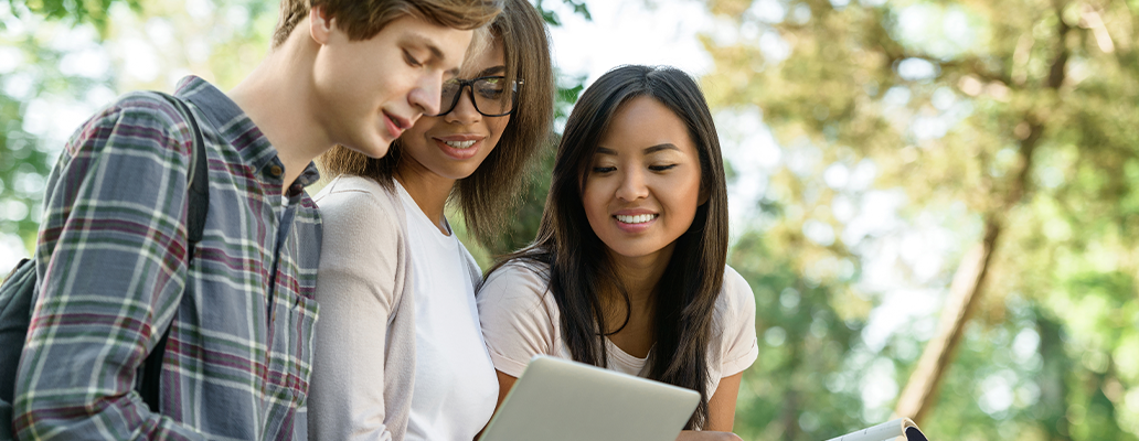 屋外でタブレットを見る3人の学生