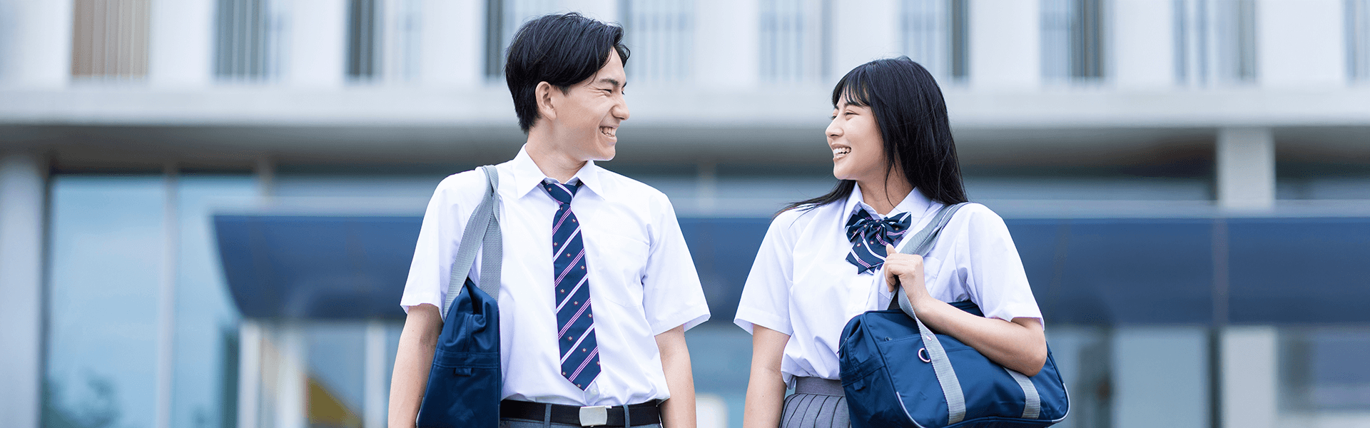 校舎前で笑顔で歩く男女の学生