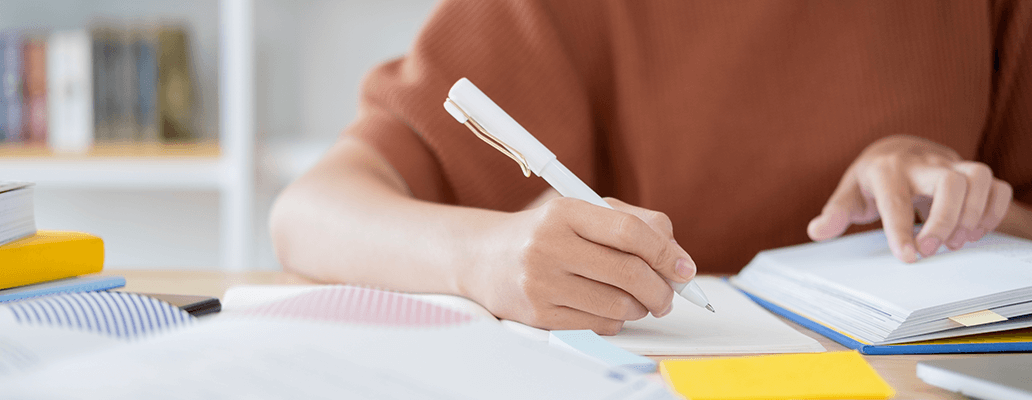 机に座ってノートに書き込む人の手元