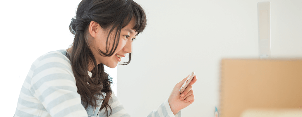 スマートフォンを手に笑顔で見つめる女子中学生