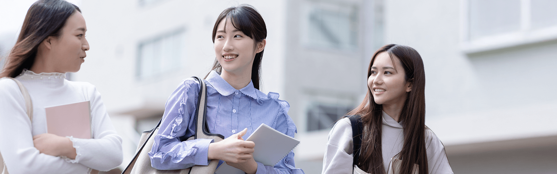 屋外でタブレットを持ちながら会話する女子学生3人