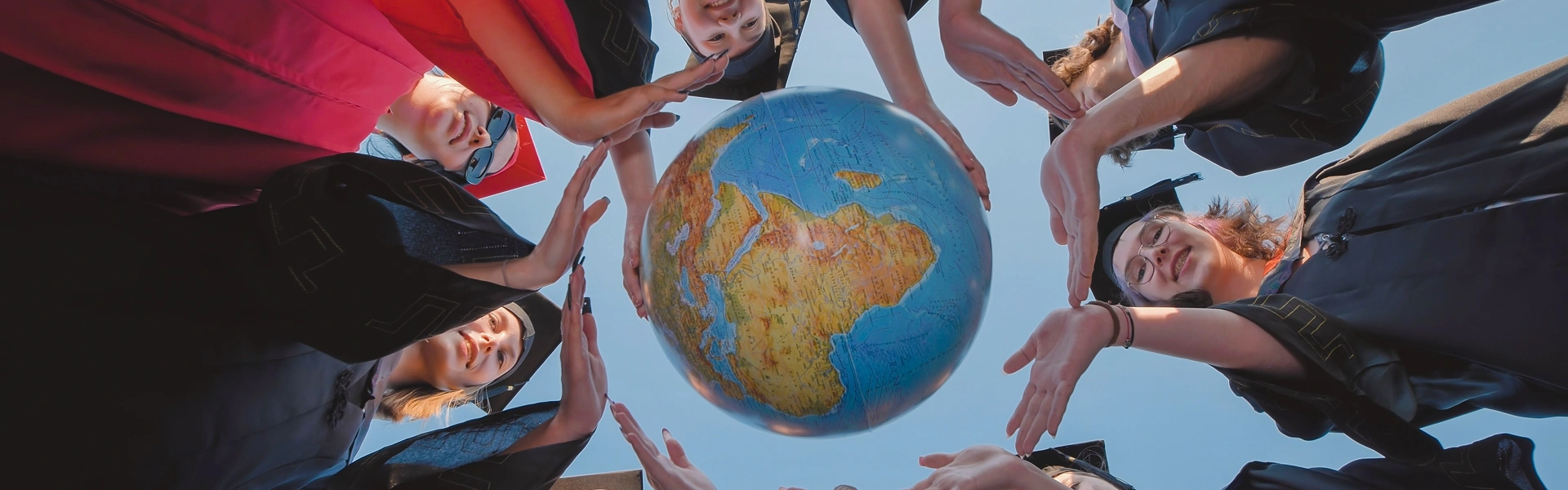 世界地図を囲んで手を伸ばす留学生たちのイメージ