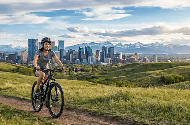 カルガリー近郊の丘から望むロッキー山脈とダウンタウンの景色、サイクリングを楽しむ人
