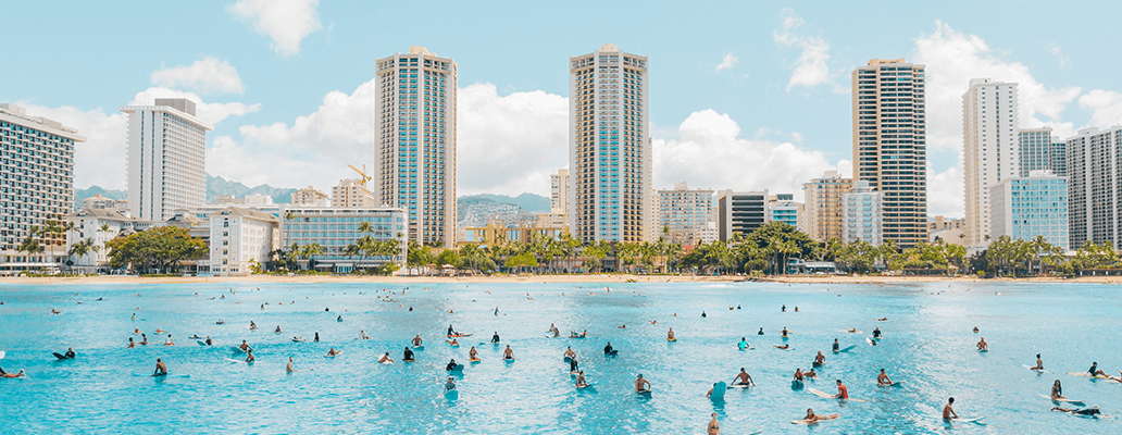 ハワイ留学の魅力 | ワイキキの海でサーフィンを楽しむ人々と高層ビルの景色