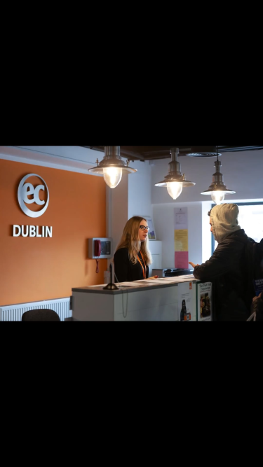 オレンジ色の壁にEC DUBLINロゴがある受付で対応する2人、屋内