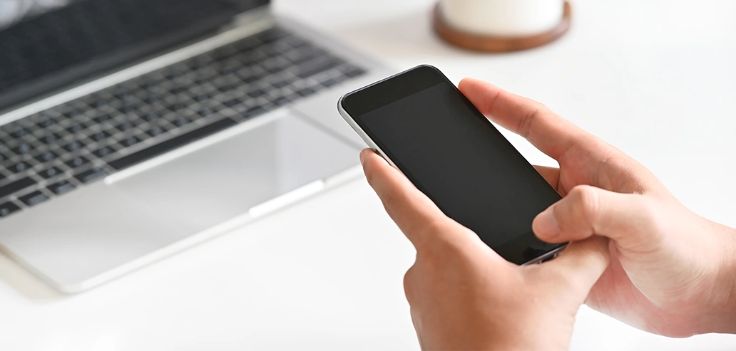 PCの前でスマートフォン操作をする手元の様子
