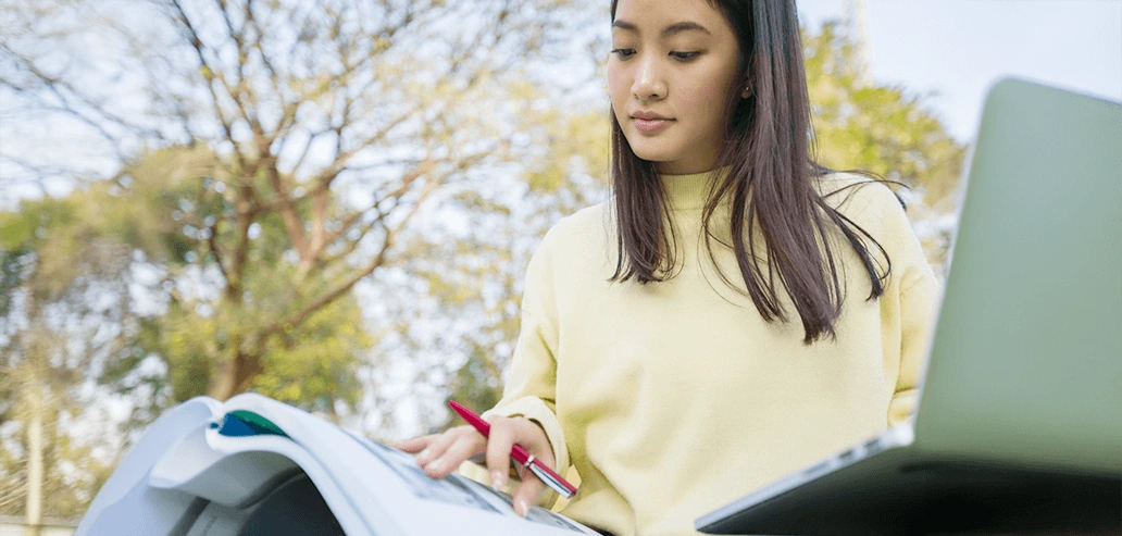 屋外でノートパソコンを使いながら勉強する女性留学生