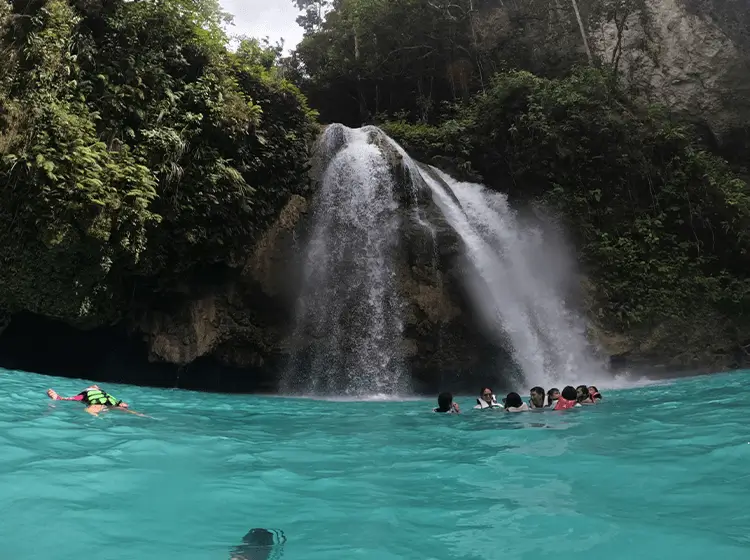 緑豊かな自然に囲まれた滝で泳ぐ人々のグループ、透明度の高いターコイズブルーの水