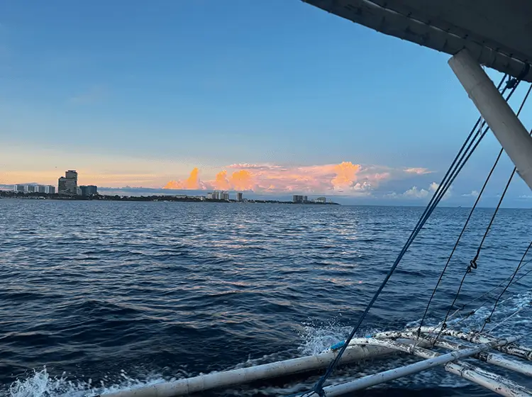 ボートから眺める夕暮れの海。オレンジ色に染まる雲と遠くに広がる街並み