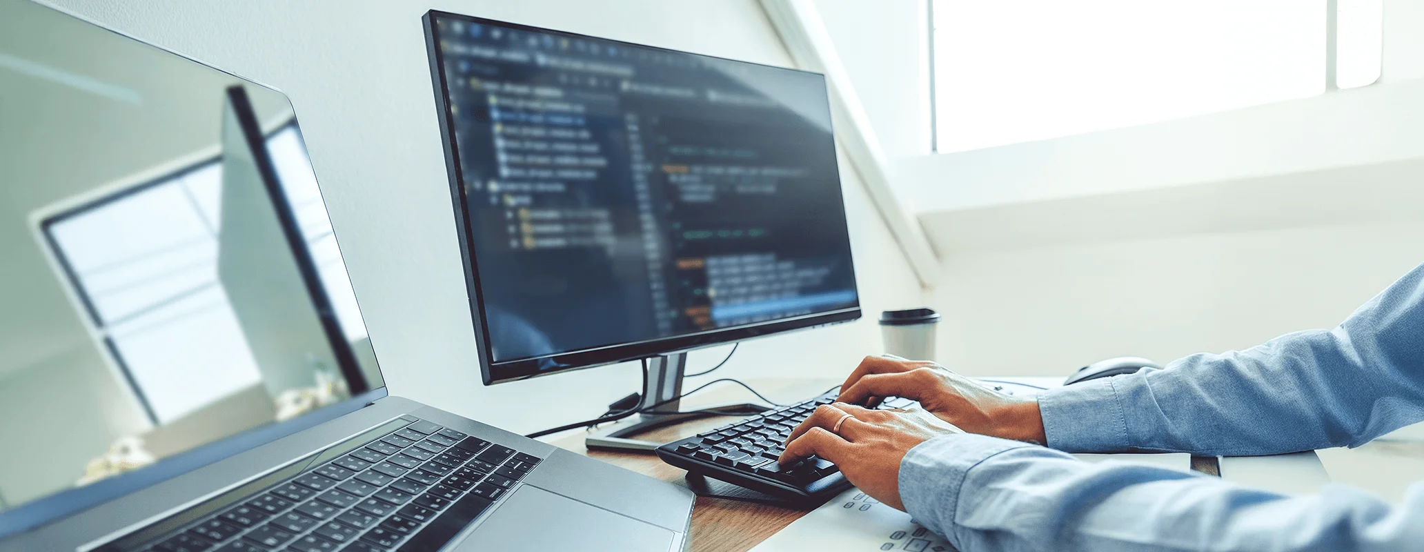 デュアルモニターでコードを書いている男性の写真