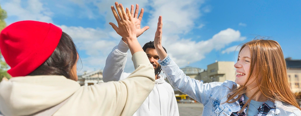 海辺で手を挙げて海外生活を楽しむ3人の若者の後ろ姿