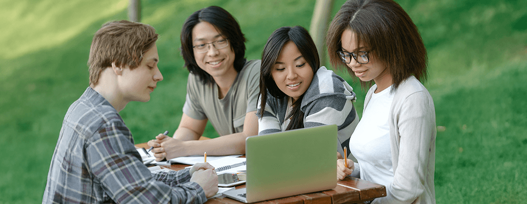 屋外のテーブルでノートパソコンを囲んで学習する留学生たち