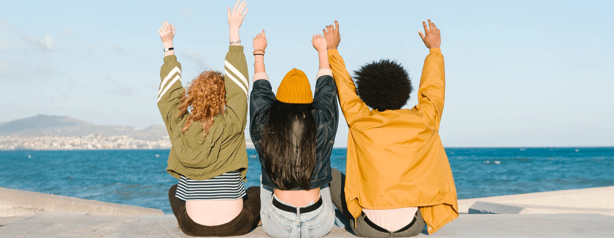 海辺で手を挙げて海外生活を楽しむ3人の若者の後ろ姿