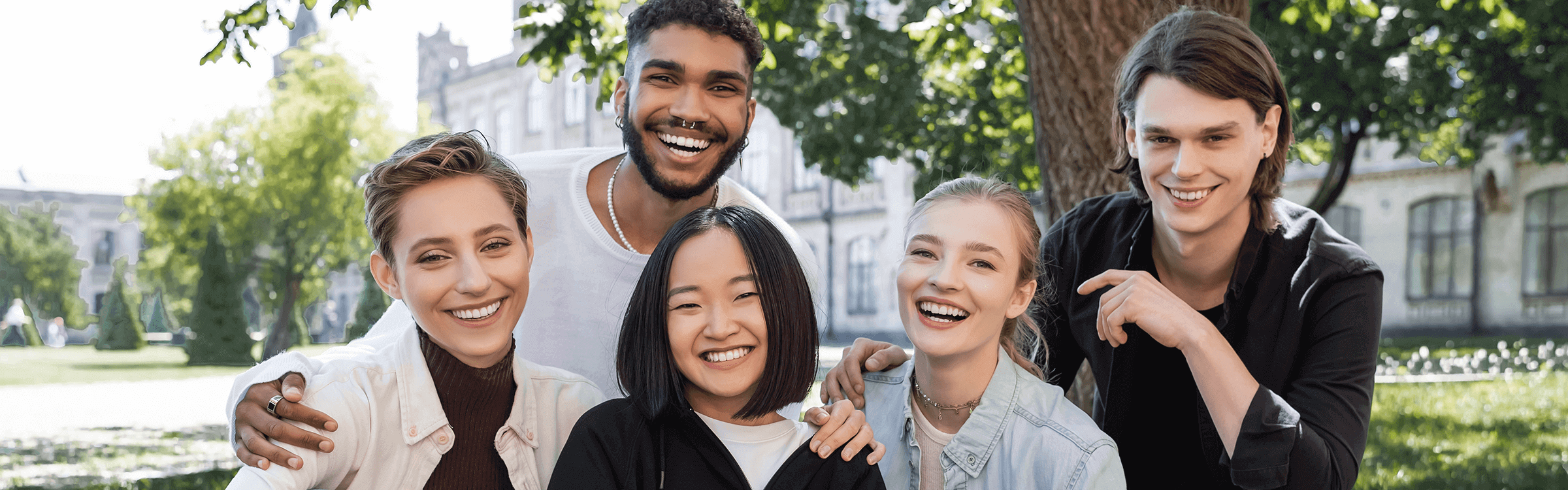 屋外で笑顔の学生グループが建物を背景に親しく会話している様子