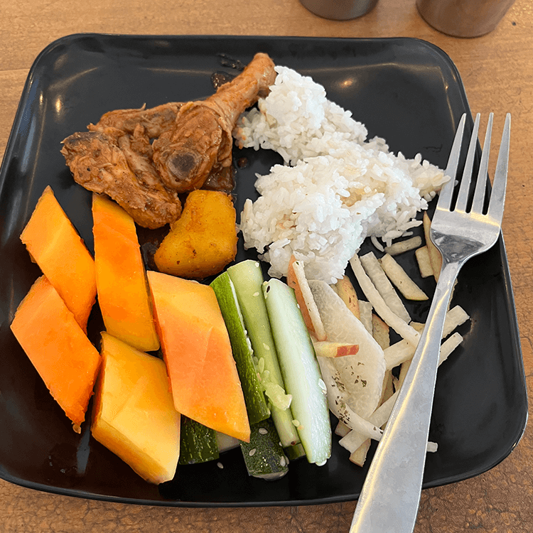 黒いプレートに盛られたフライドチキン、ライス、野菜の食事