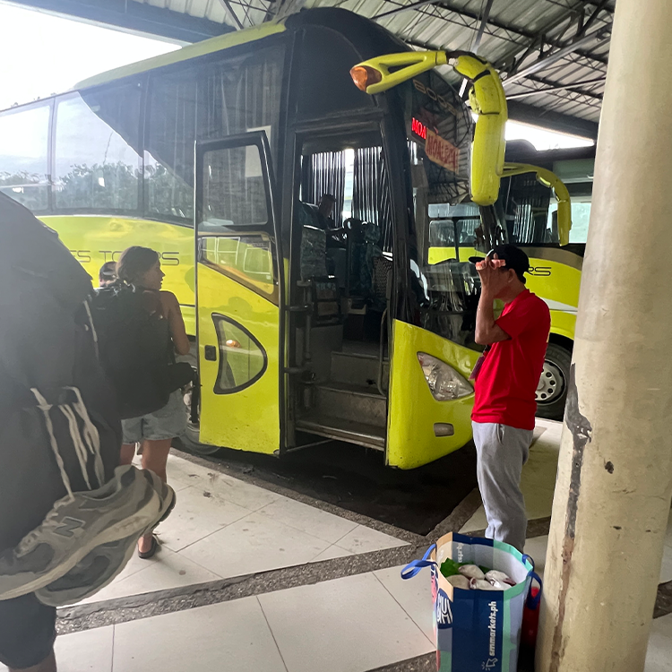 黄色いバスの前で赤いシャツを着た男性が立つ屋内のバス停