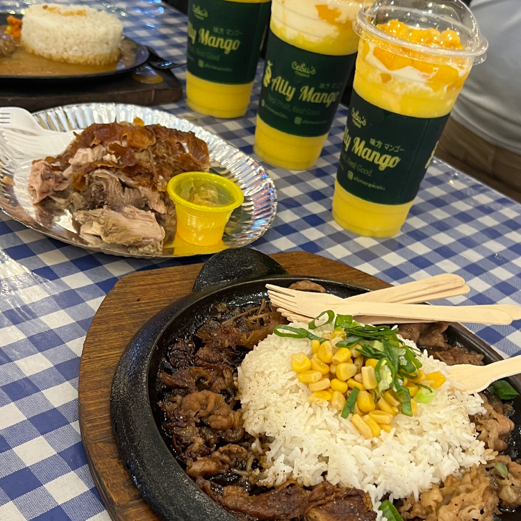 鉄板料理とマンゴードリンクが並ぶチェック柄テーブルクロスの食事