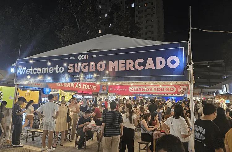 賑わうSUGBO MERCADOのウェルカム看板と夜市の人々