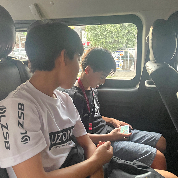 車内で二人の学生が座ってスマートフォンを見ている