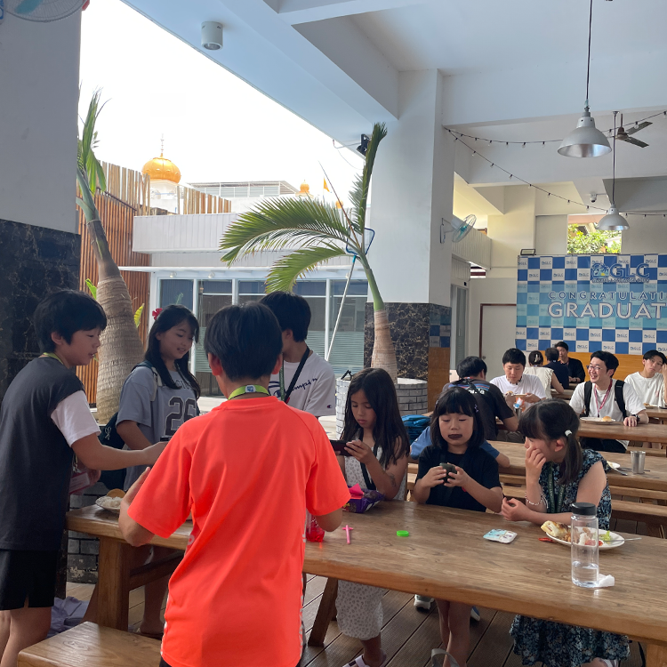 屋外テラスで学生グループが木製テーブルを囲んで食事をしている