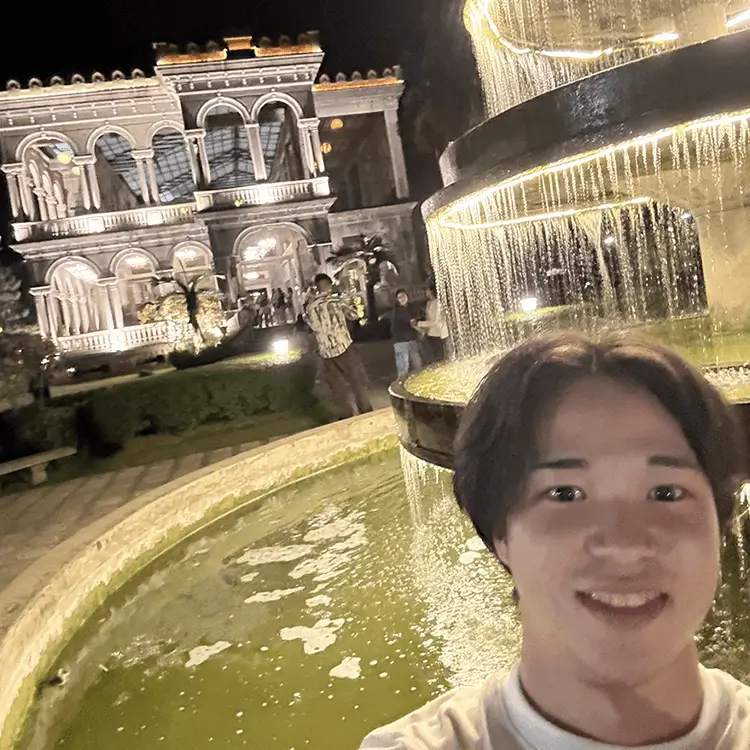 夜の噴水と歴史建築を背景に笑顔でセルフィーを撮る男性