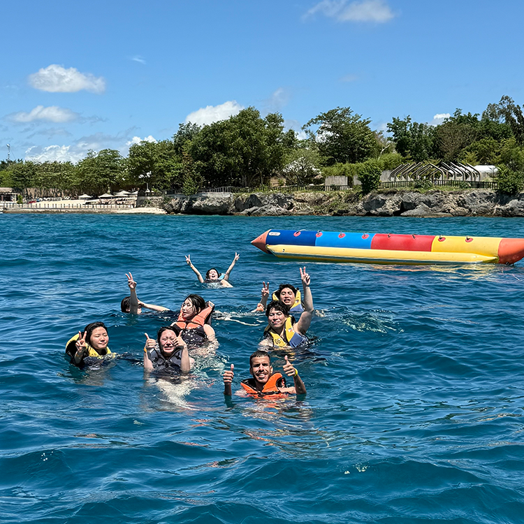 海で泳ぐ8人のグループ、バナナボートの近くで手を上げて笑顔