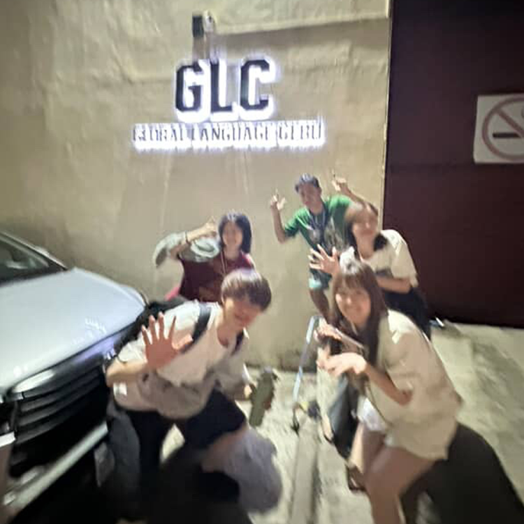 GLCの看板前でポーズを取る学生グループ、笑顔を見せる人々