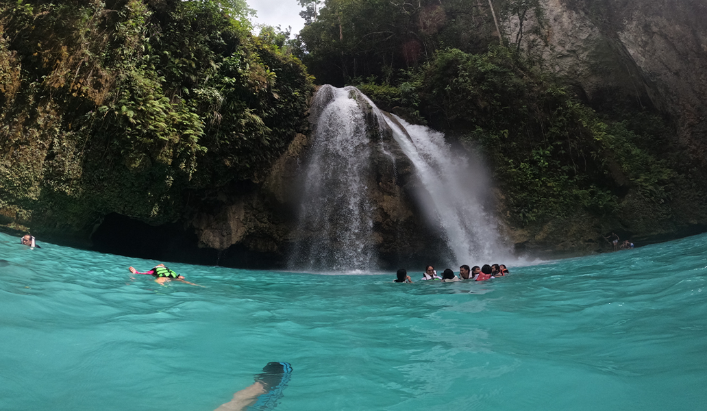 緑豊かな自然に囲まれた滝で泳ぐ人々のグループ、透明度の高いターコイズブルーの水