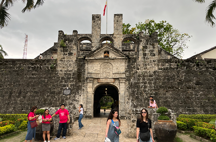 石造りの歴史的な建物の前で人々が観光している屋外の景色