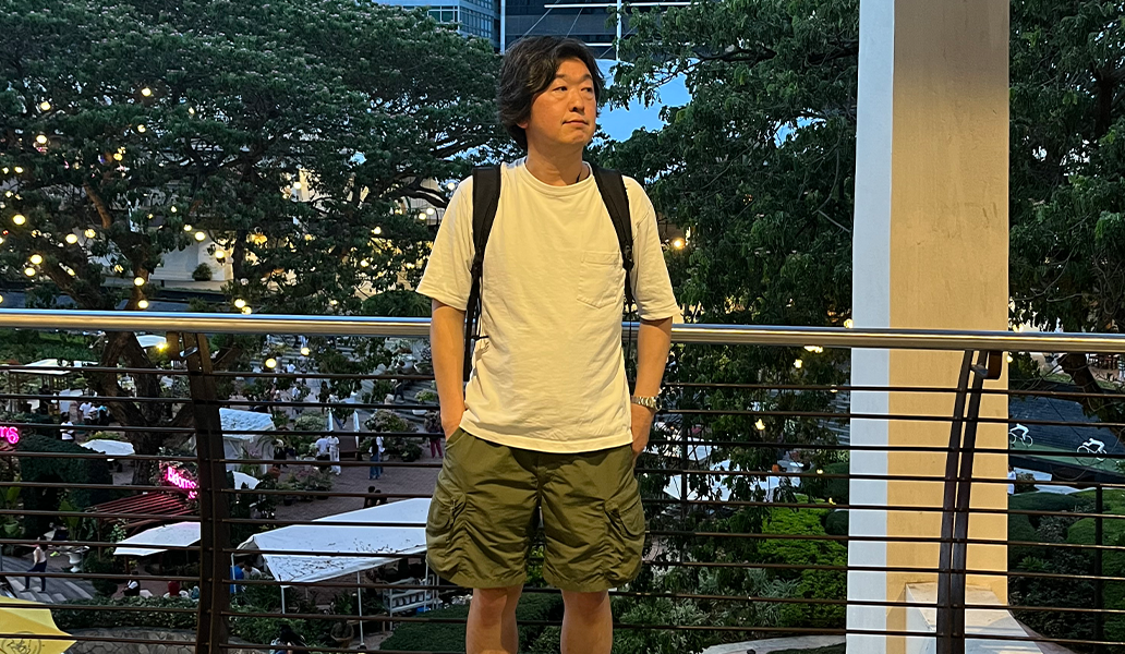 バックパックを背負った男性が屋外のバルコニーで緑の景色を背景に立っている