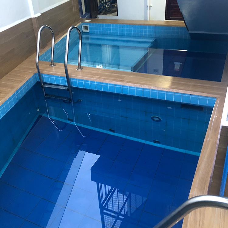 青いタイルの屋内プールと金属製の手すりがある建物内部