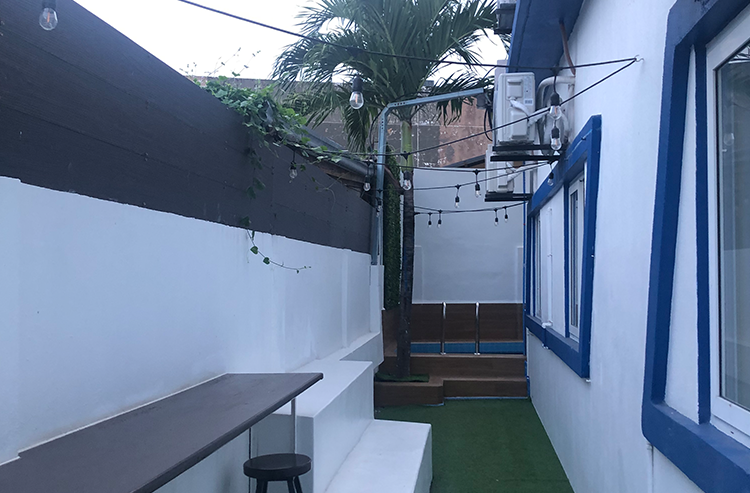 白い壁と青い窓枠の屋外中庭、ヤシの木と緑の人工芝がある建物