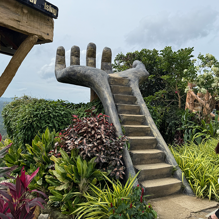 大きな石の手の彫刻に階段が通っている屋外の自然景色で熱帯植物に囲まれている