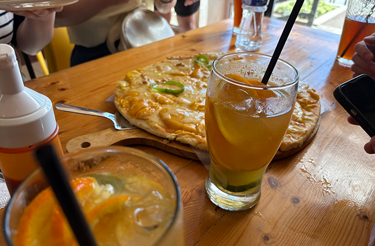 木製テーブルの上にピザとドリンクグラスとスープがある食事の風景