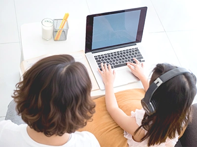 自宅でオンライン英会話に取り組むヘッドセットを付けた小学生と保護者