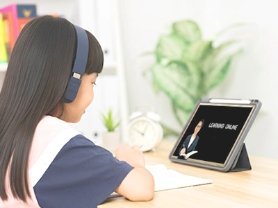 タブレットでオンライン英会話レッスンを受けるヘッドホン姿の小学生