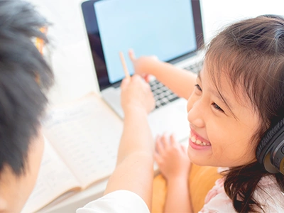 パソコンでオンライン英会話レッスンを受けながら笑顔で学ぶ小学生の女の子