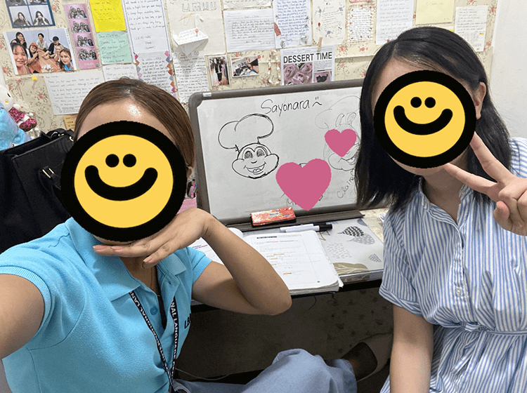 教室で笑顔の学生二人がピースサインをしながらホワイトボードの前でポーズを取っている