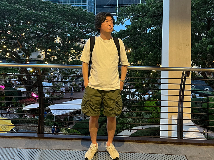 バックパックを背負った男性が屋外のバルコニーで緑の景色を背景に立っている